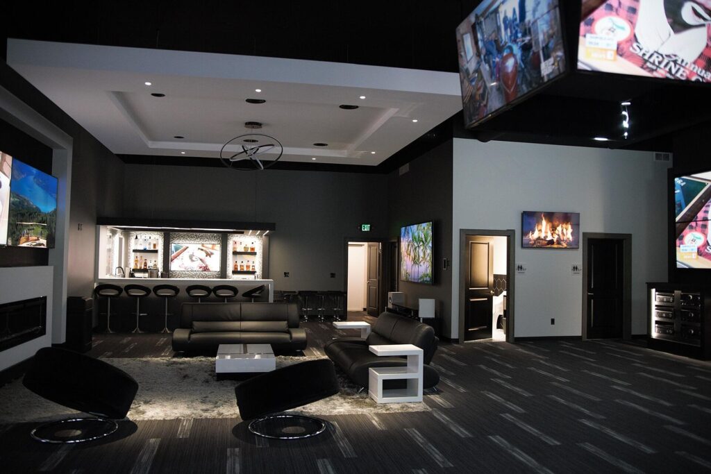 A modern lounge with a sleek, black and gray interior featuring a bar area with illuminated shelves stocked with liquor bottles. _ Pure AV Luxury Home Automation.jpg